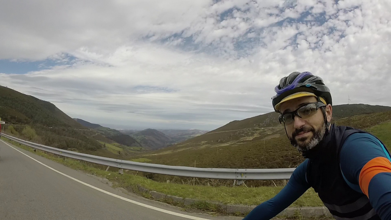 Me, looking at the camera and behind the whole view from alto da garganta with the valley, hills on both sides and at the end of it, like in the end of a tunnel, the cantabric sea. The sky is mostly cloudy, with some holes that let you see the blue behind the clouds