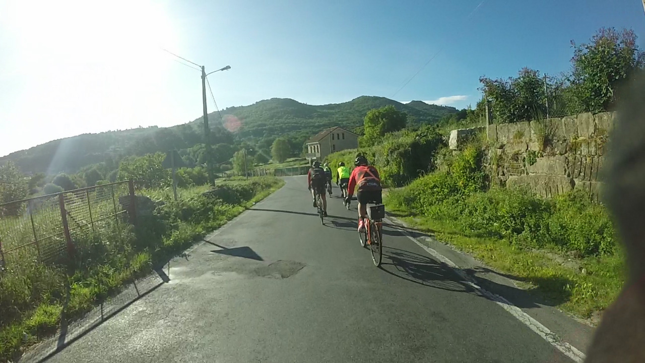 Our little group of randonneurs, going down a small road towards some hills under a blue cloudless sky