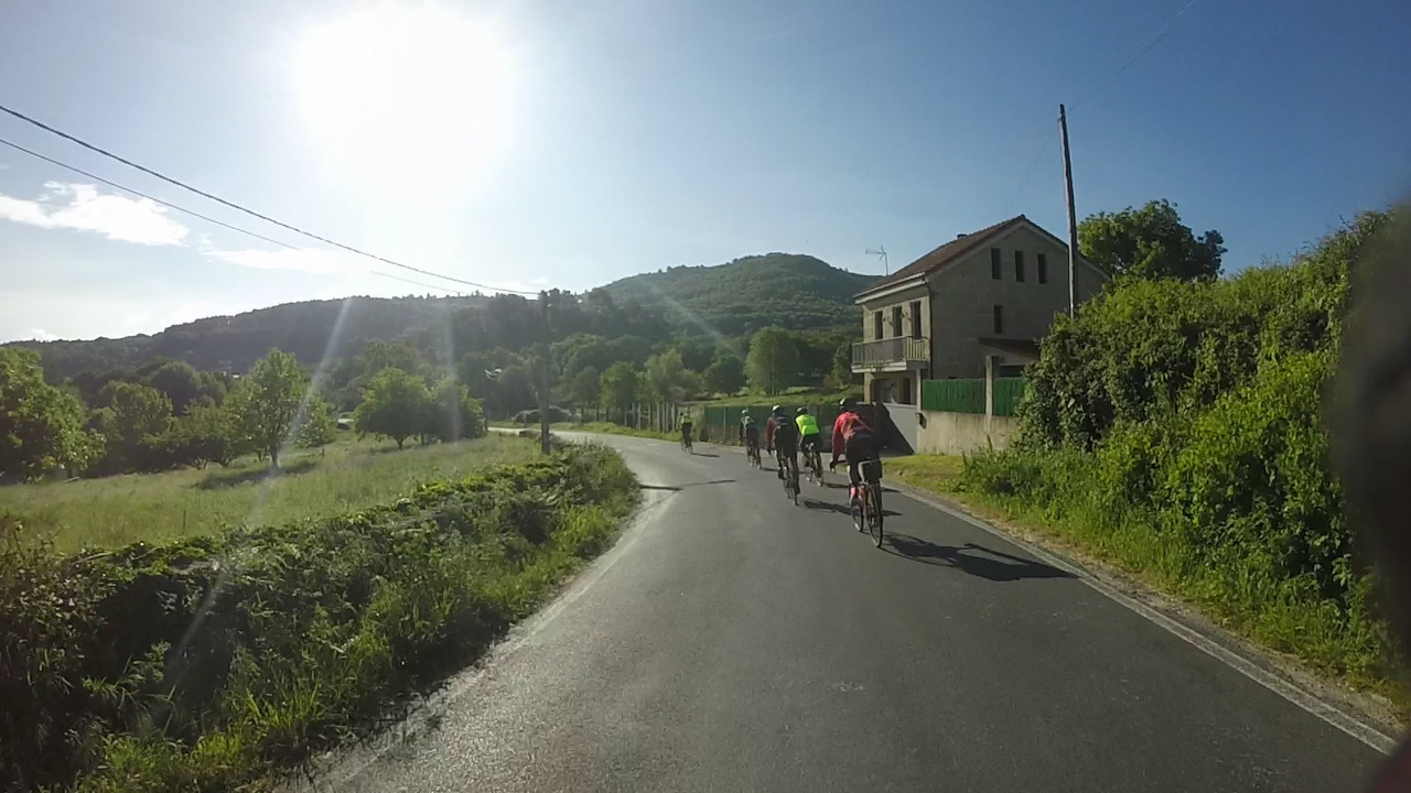 Our little group of randonneurs, going down a small road, passing another small stone house under a blue cloudless sky