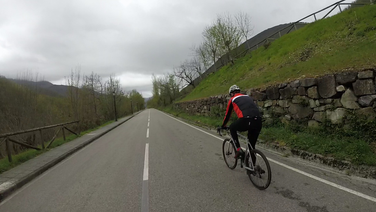 Juankar riding on the right lane of a long road, alongside a stone wall