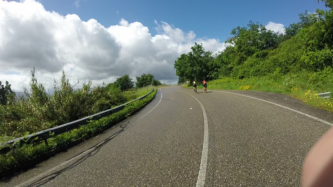 A few randonneurs from my group, going up a road. There are a few clouds, but it is mostly sunny and the road is drying up
