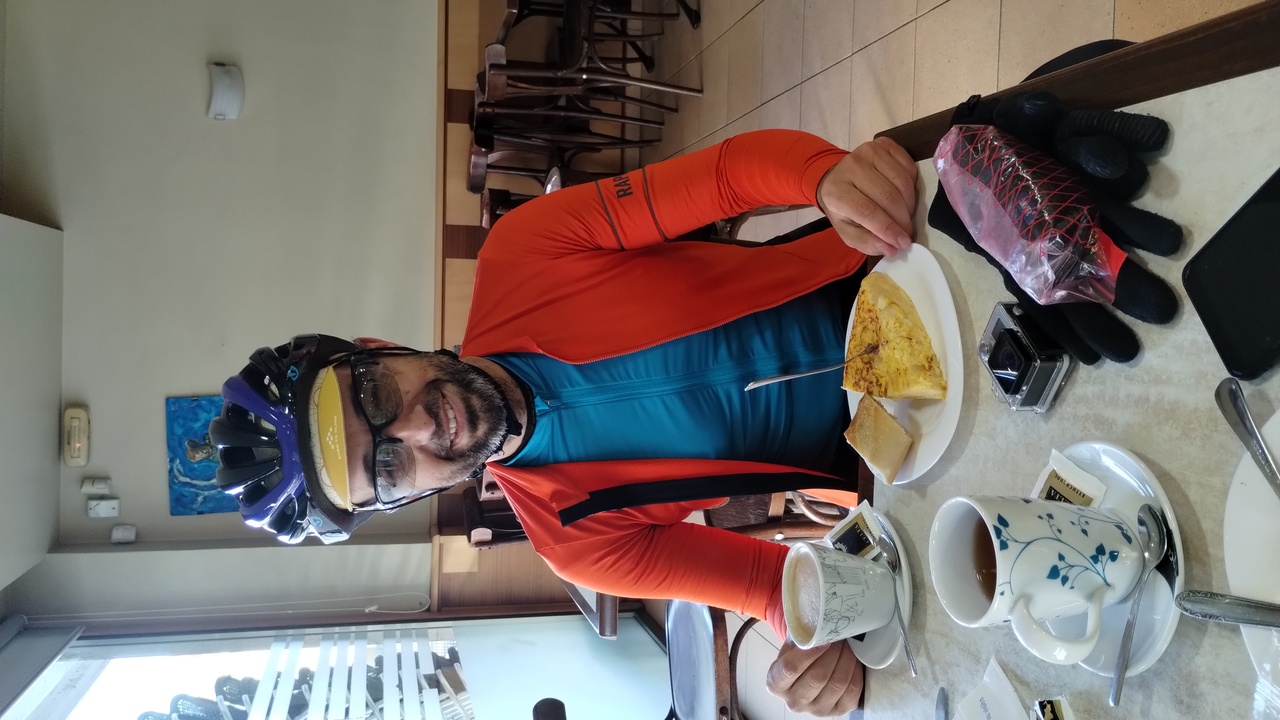 Picture of myself, sitting in the cafe in Allariz, I've a coffee and a big piece of tortilla in front of me, as well as my gopro, gloves, etc