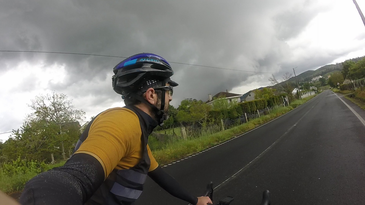 Picture of myself, taken from my right side, there is a big dark grey cloud behind me and the road turns left towards it