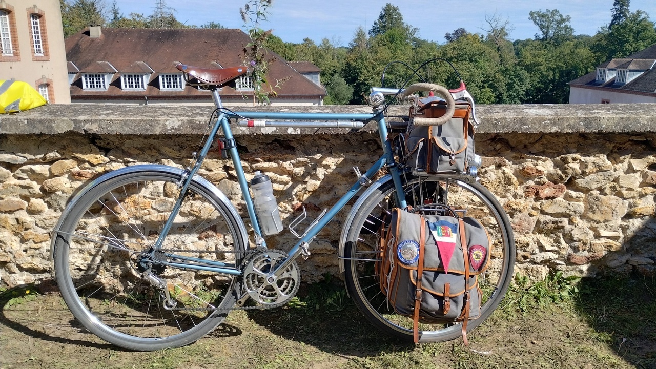 A beautiful old-school steel bike, blue, with what looked like an old Campagnolo drivetrain with triple chainrings, shifters on the frame, leather saddle, and big bags on the handlebars and fork panniers
