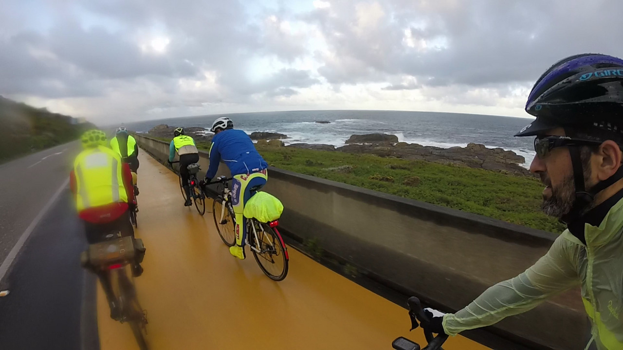 Riding behind a group of several randonneurs, riding in pairs on the bike lane by the coast, under the rain