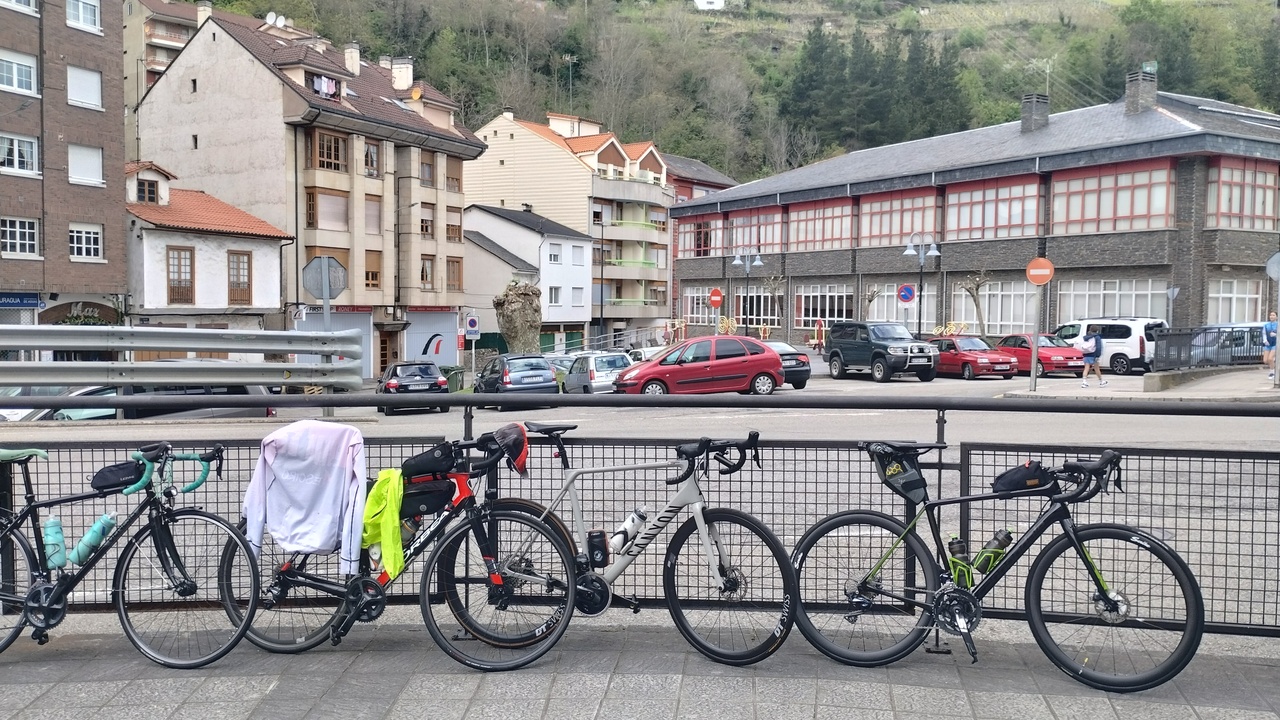 Several of our road bikes, leaning on a fence with a road and some houses behind them