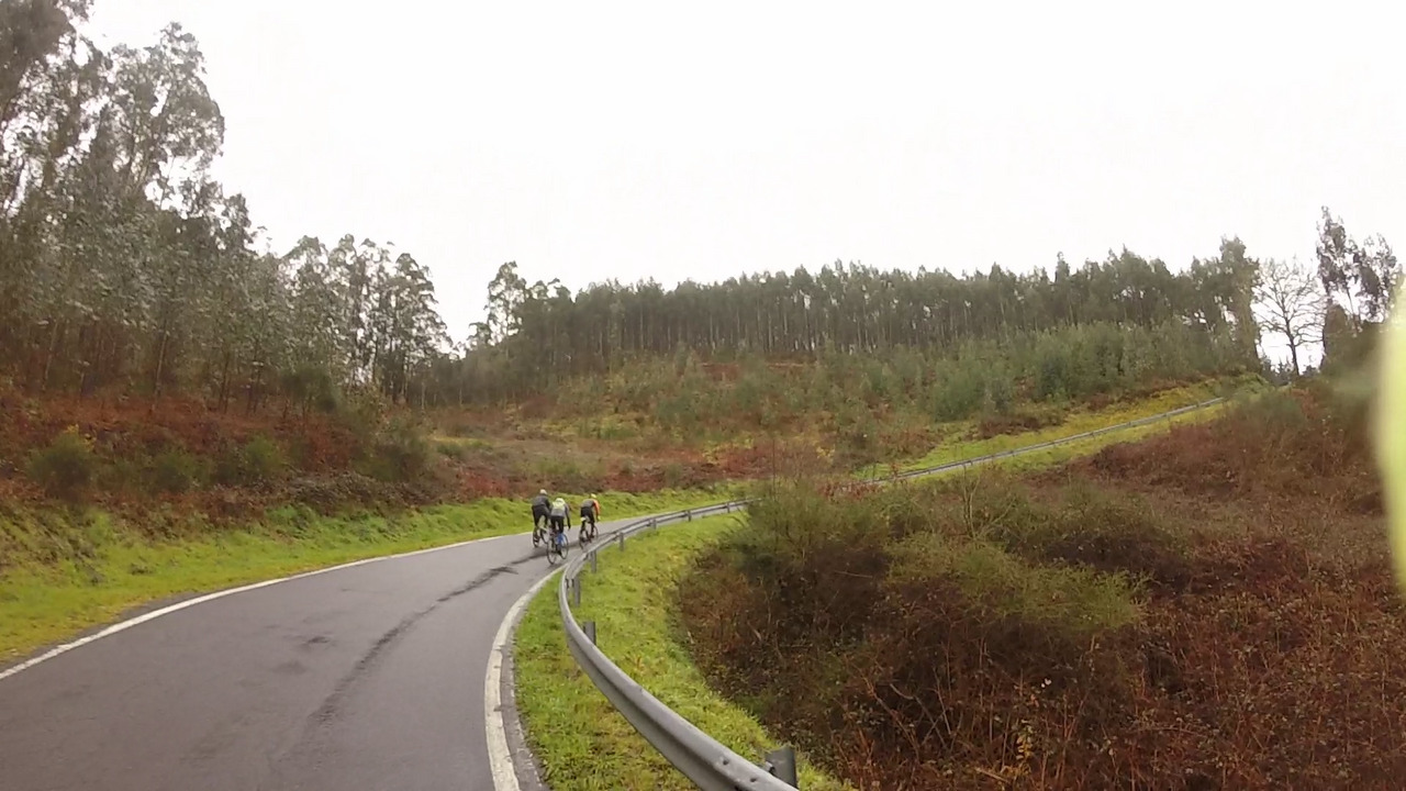 Three cyclists at a distance, going up a hilly road