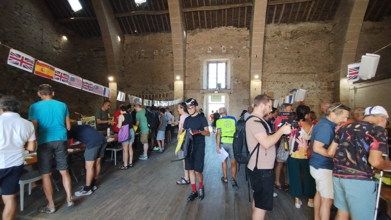 Entering one of the buildings for the documentation pick-up. Three are 2 lines of tables on both sides, each of them with a line of flags over them. Lots of people are both at the tables and walking around.