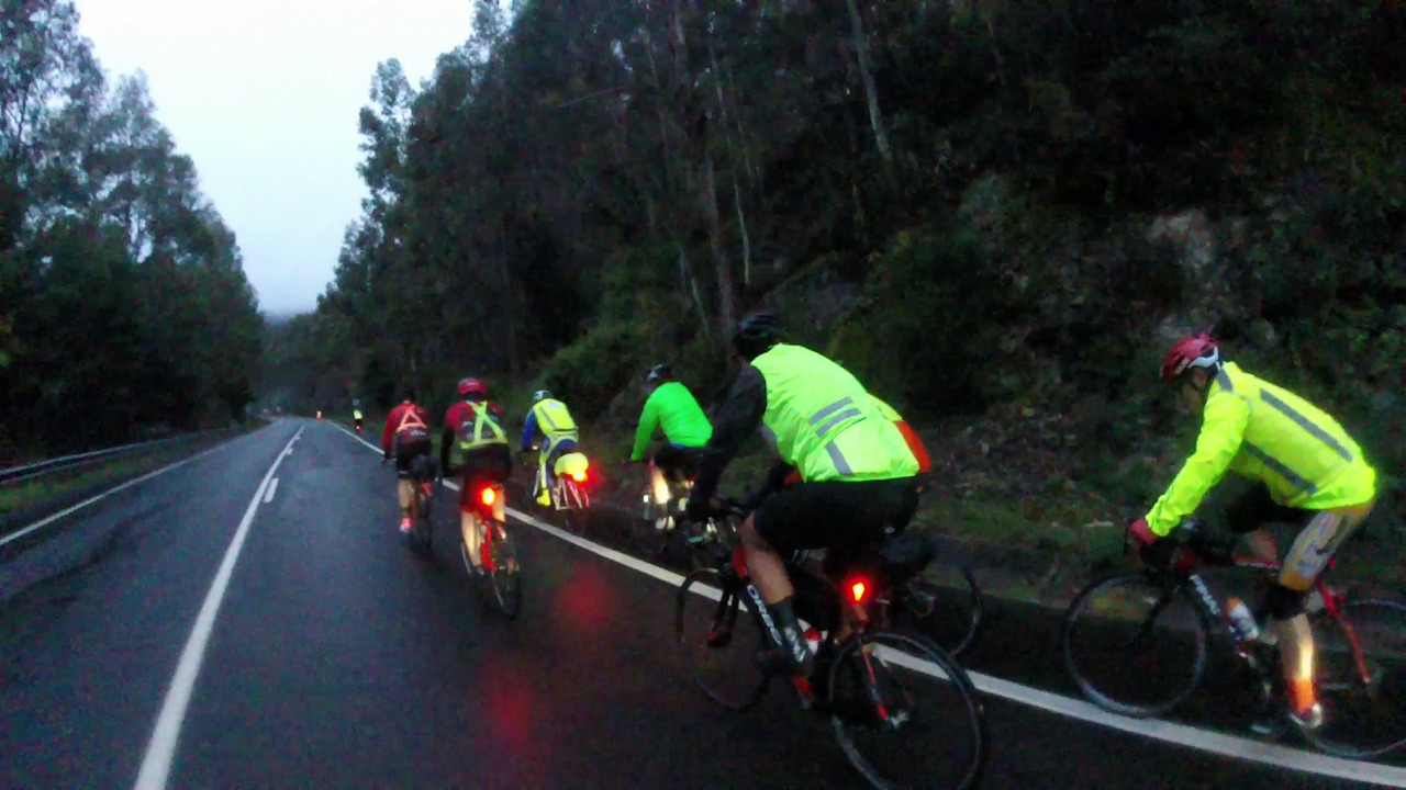 A group of randonneurs, riding in pairs up the first climb of the day, under some strong rain