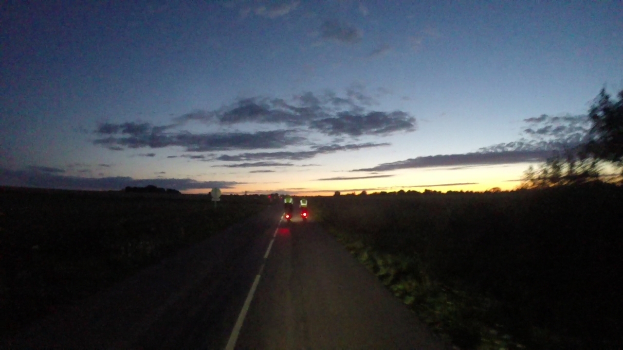 A couple of tail lights, riding towards sunset. Some more cyclists can be seen at the back of the photo