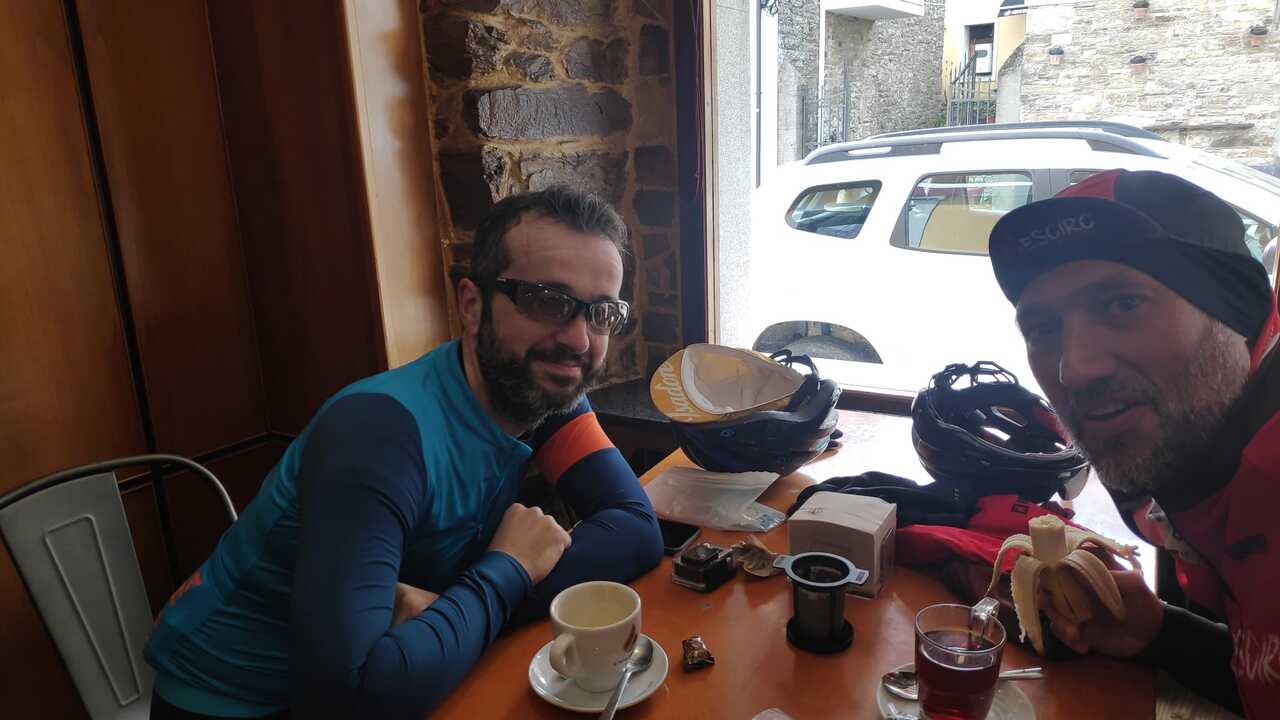 Dani and me sitting at a table in Cafe Demetrio in Fonsagrada, in the first coffee stop of the day, latte for me, black tea for him. Our things are scattered around the table.