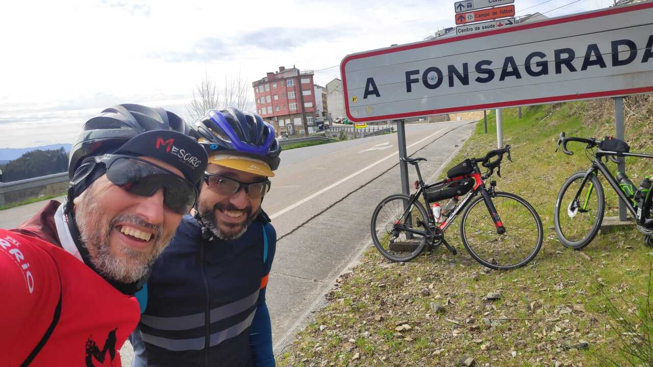 Dani and me together, by the sign with big letters 'Fonsagrada' at the exit of the village. Both bikes are leaning against the sign and Fonsagrada can be seen on the back.