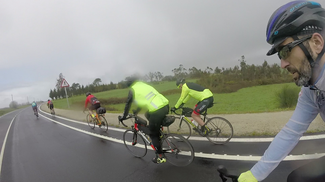 Everybody on camera, riding our bikes under the rain, the picture is a bit foggy and has rain drops all over, due to the rain falling on us