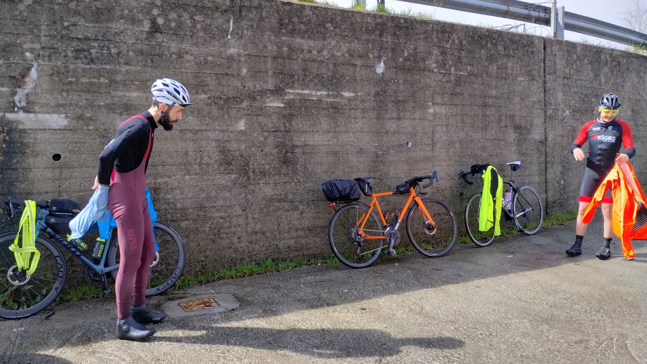 Alex and Oscar removing some layers and hanging them for drying, with their bikes leaning against a concrete wall