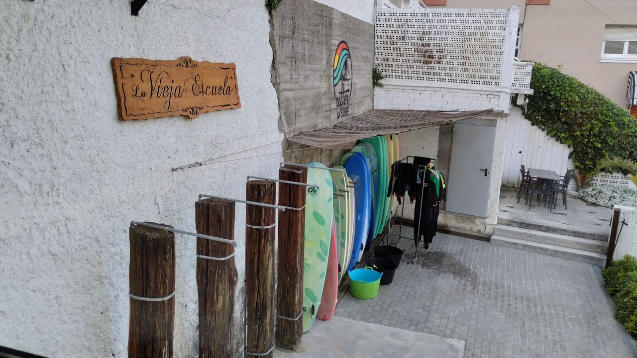 A few surf boards leaning on a wall, under a wooden sign 'La Vieja Escuela', which is the surfing school from the guys at After Surf
