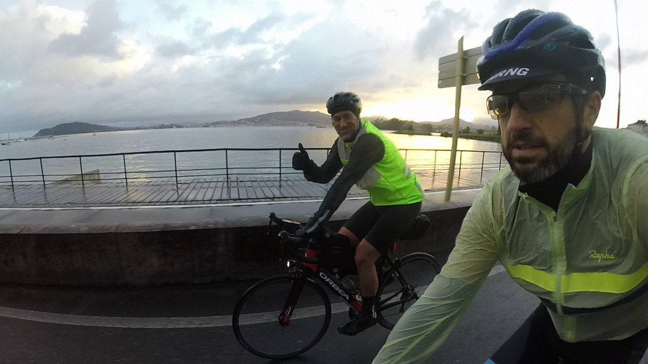 Dani, leaving Baiona on the road that goes by the Atlantic Ocean. Behind Dani there is the Atlantic and the sun is rising from behind some hills there