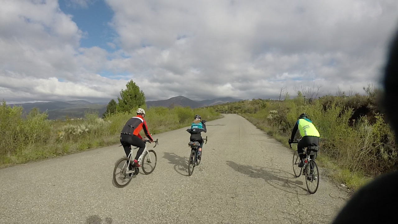 Juankar, Estefanía and Xacobe on their way up to the open sky mine, riding on a bit broken road with an open view of Fabero from above to their left.