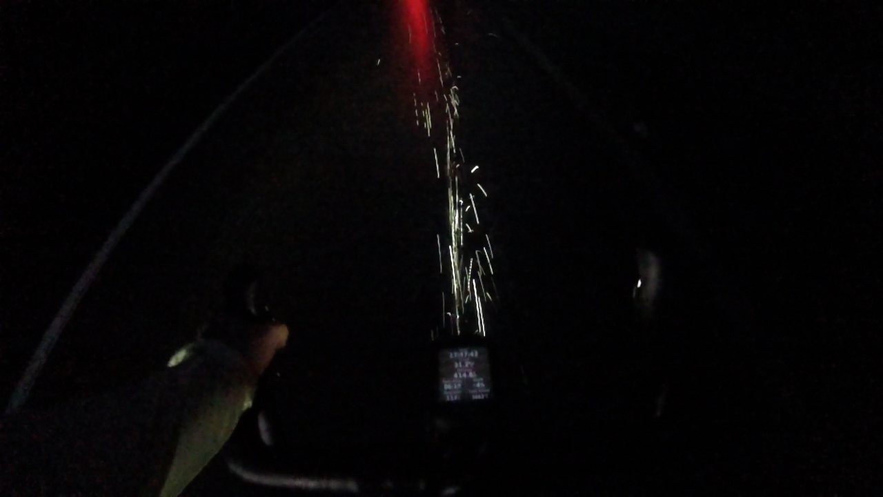 Photo of my handlebars under the rain at night. My headlight beam makes the water sprayed from my front wheel to look like welding sparks