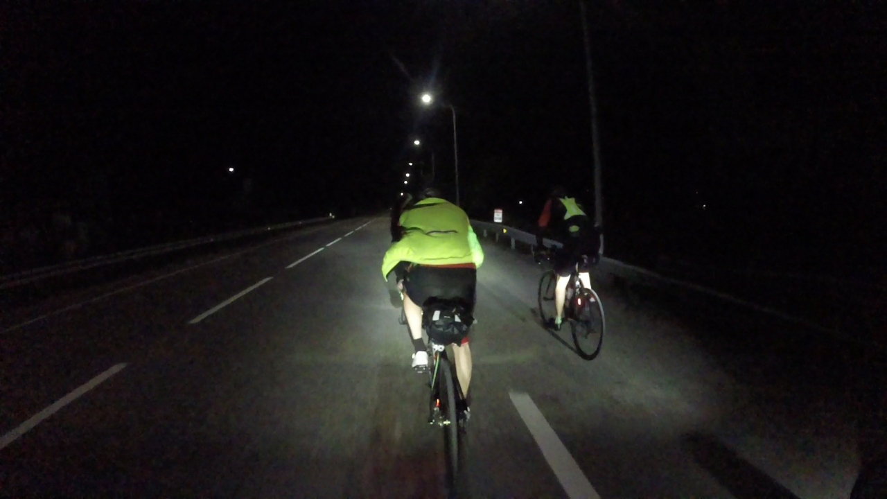 Jose and Oscar, riding in front of me, on a straight road with lots of street lamps on its right side