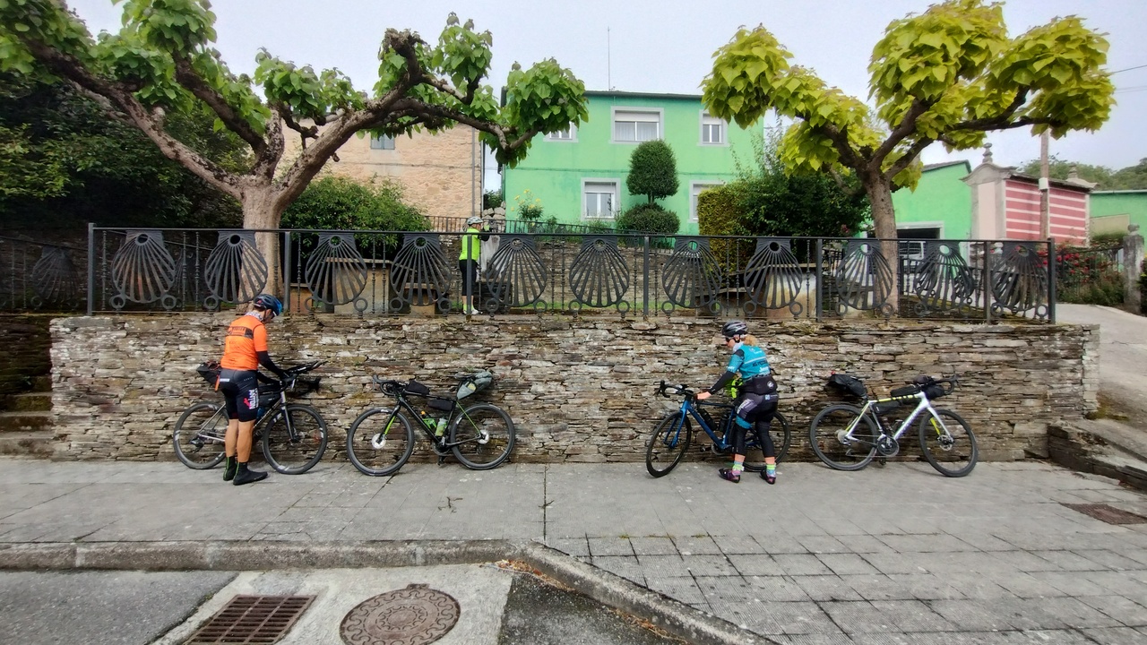 Our bikes, leaning on the wall below the fountain at paradela. Roberto and Estefanía are picking up stuff from their bags, while Valentín is refilling his bottles