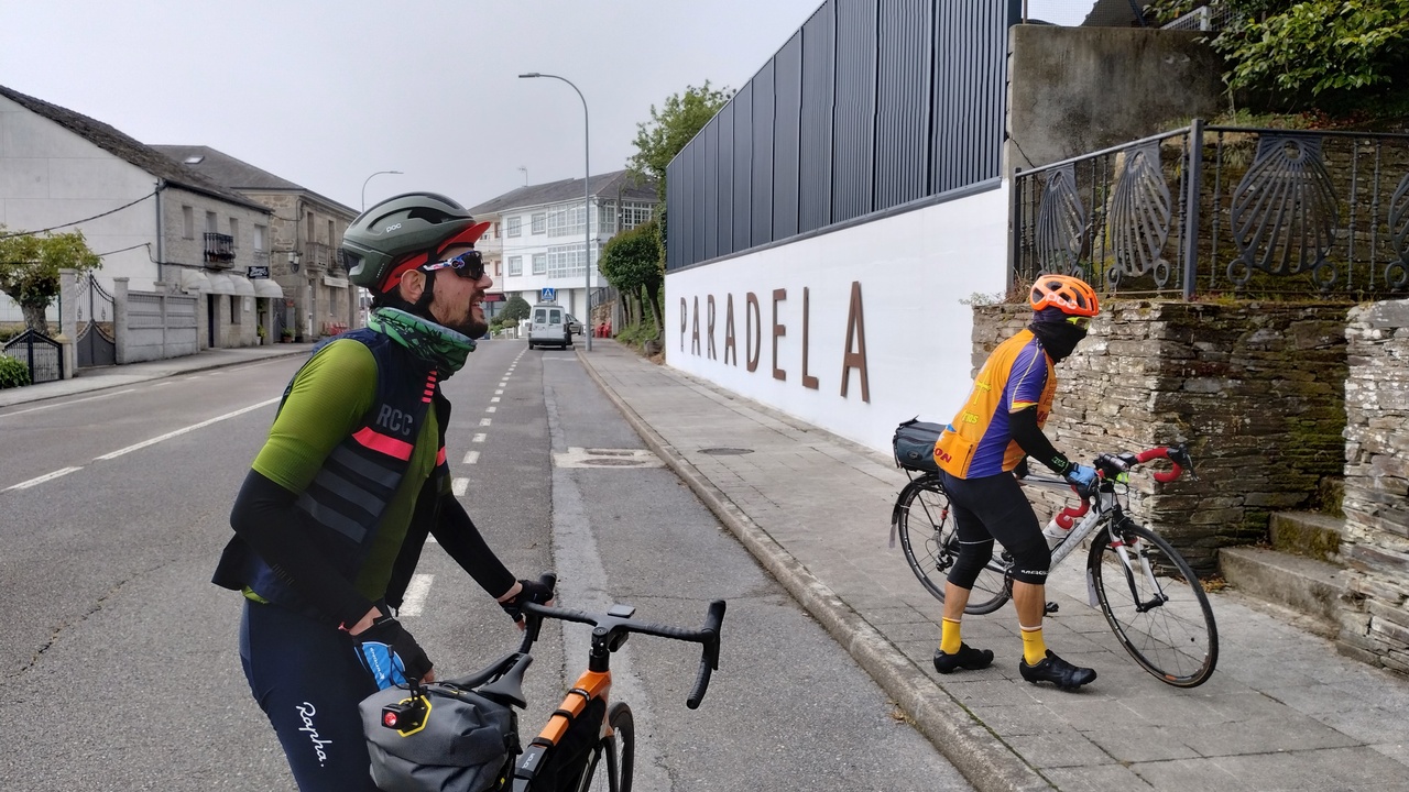 Sergio and Saúl, holding their bikes, by the big letters on a wall: P A R A D E L A