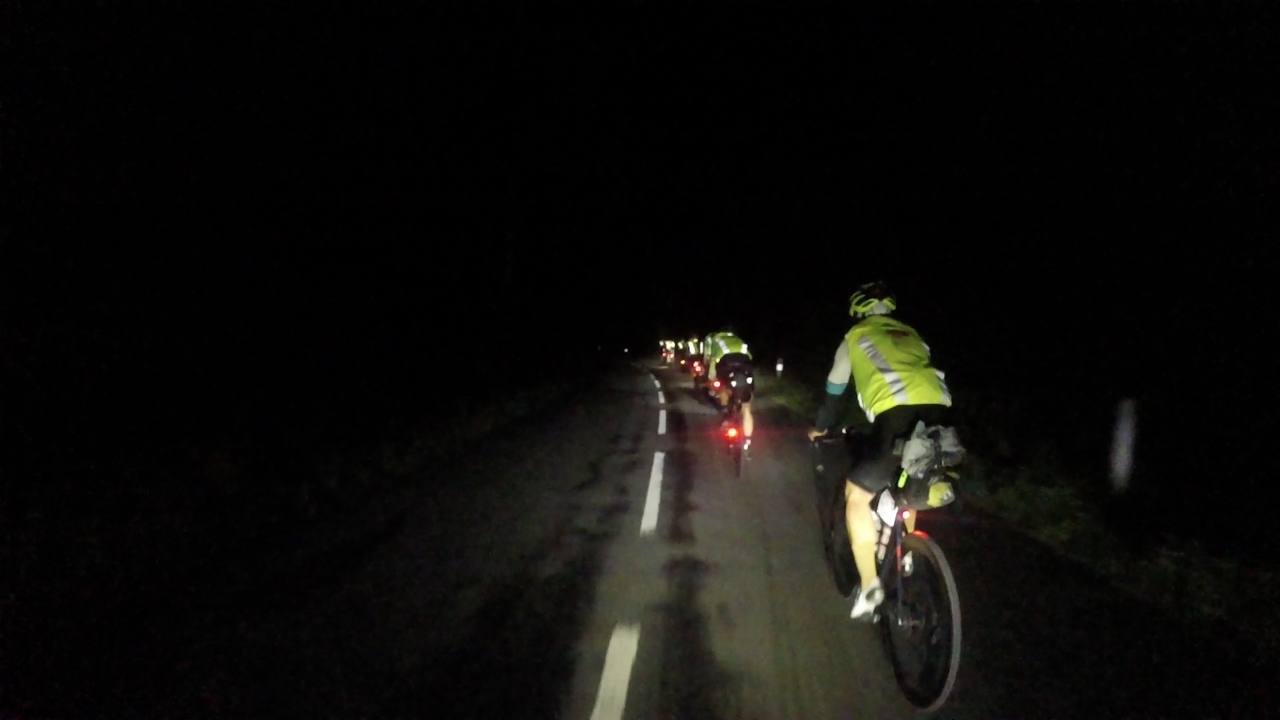 A queue of randonneurs wearing reflective vests riding towards Villaine La-Juhel on sunday night