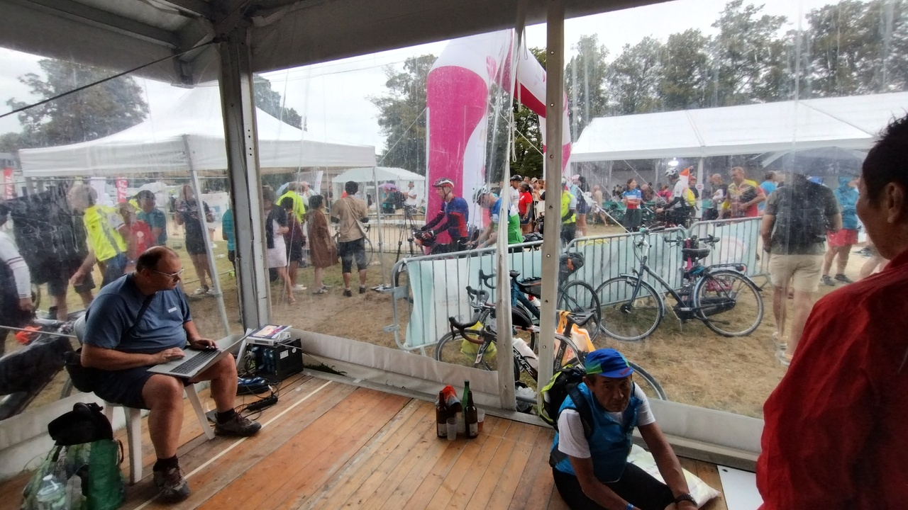Some randonneurs inside one of the tents, some other outside, watching the arrival of more riders