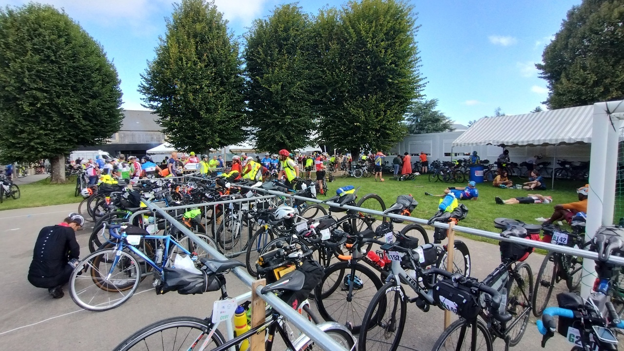 Lots of bikes parked in Tintèniac, randonneurs laying on the grass by the parking