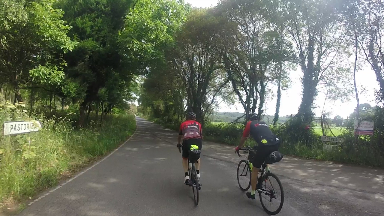 Jose and Oscar, entering a zone covered by trees on our way to A Pastoriza. On the left of the picture there is a road sign in the shape of an arrow saying 'Pastoriza'
