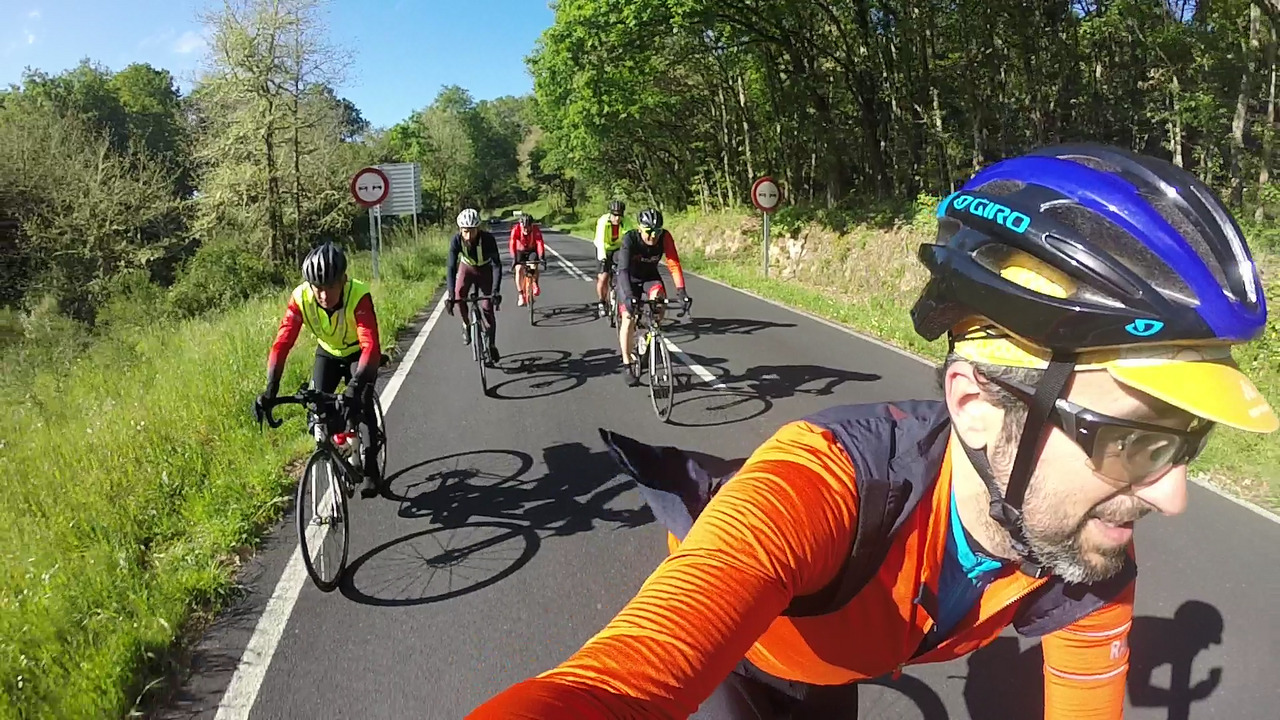 Selfie of the whole group riding on the road towards Alto do Couso, green trees on the right of the picture, grass on the left