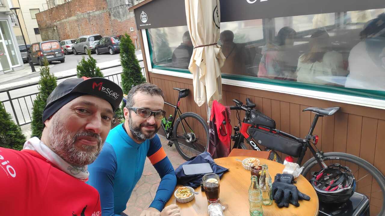 Dani and me at a table, outside, having our mini-lunch of the day. Coca cola, pasta salad and a small bocadillo. Our bikes are leaning against a wooded panel/wall behind us
