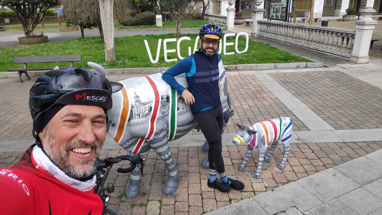 Dani and me, with the sign that says 'Vegadeo'. Near the sign are two sculptures of a cow and her calf. I'm leaning on the cow while Dani takes the selfie photo